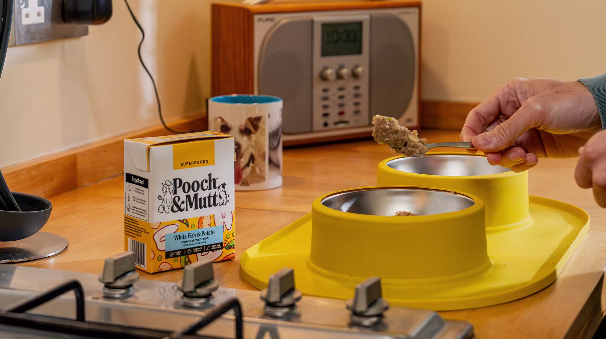 A shot of a dog owner's hand as they spoon Pooch & Mutt's White Fish & Potato Wet Food into yellow dog food bowls.