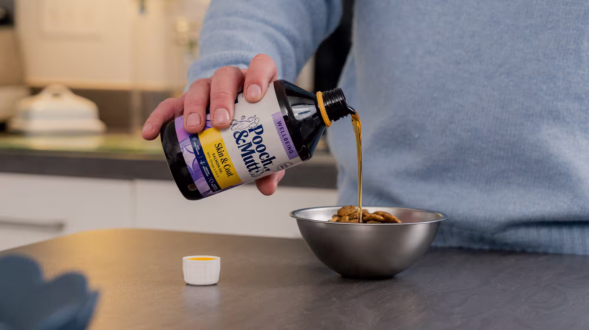 Dog owner pouring Pooch & Mutt's Salmon Oil over dog kibble in a silver metal bowl.