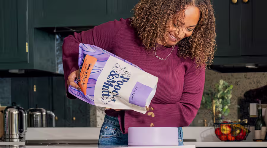 A dog owner pouring Pooch & Mutt's Slim & Slender Dry Food into a dog bowl.