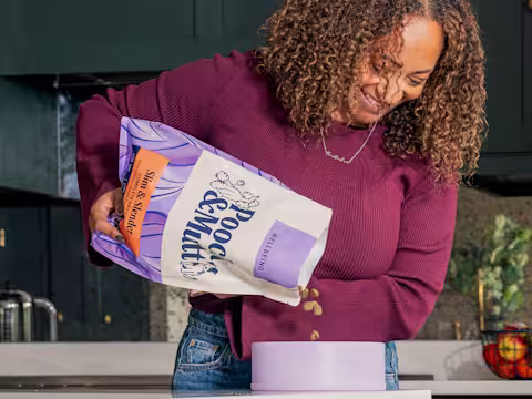 A dog owner pouring Pooch & Mutt's Slim & Slender Dry Food into a dog bowl.